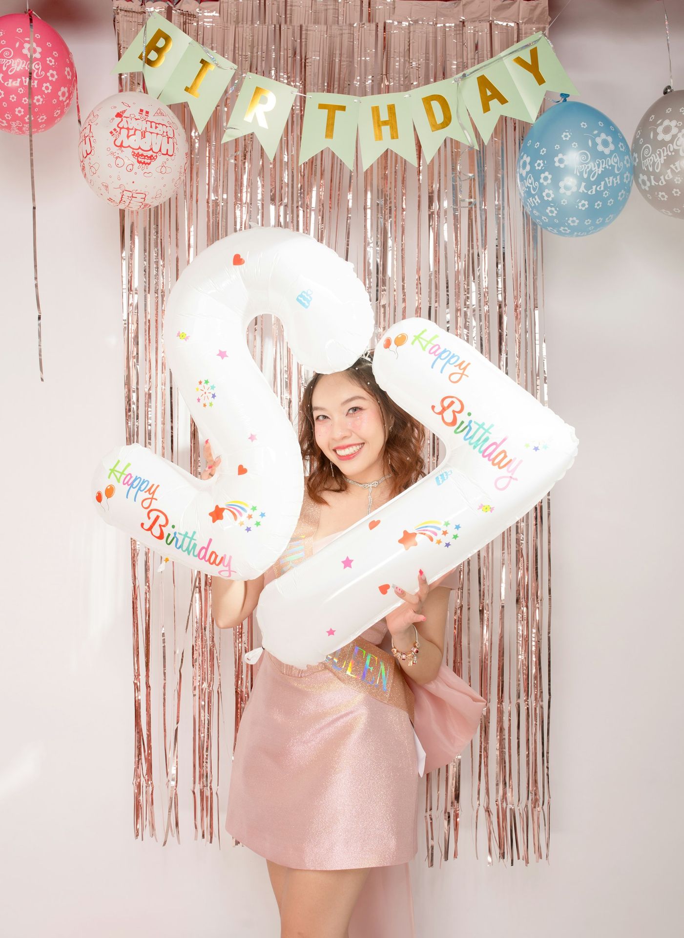A woman holding a large number balloon in front of a birthday banner